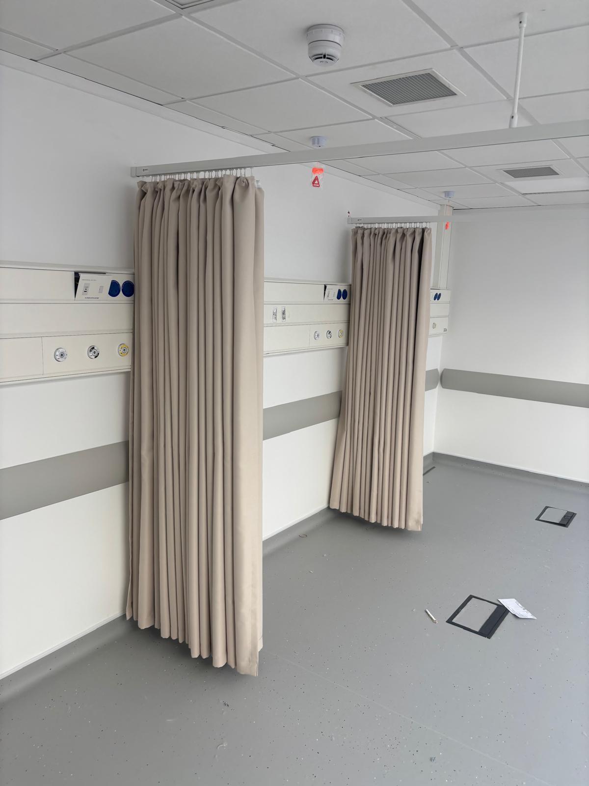 NHS ward bay with cream cubicle curtains and bedhead trunking